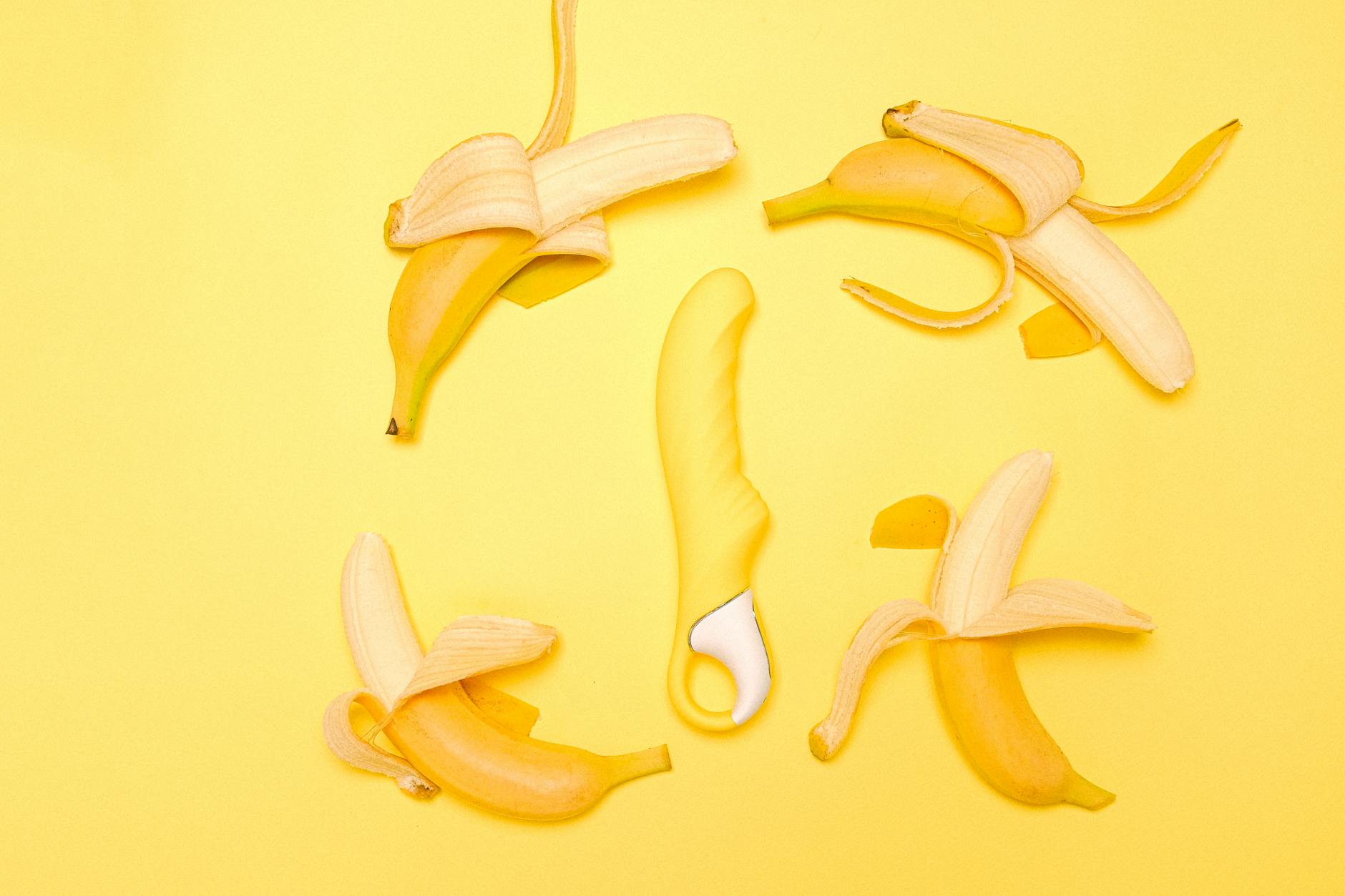 A yellow lemon clitoral vibrator surrounded by peeled bananas on a bright yellow background