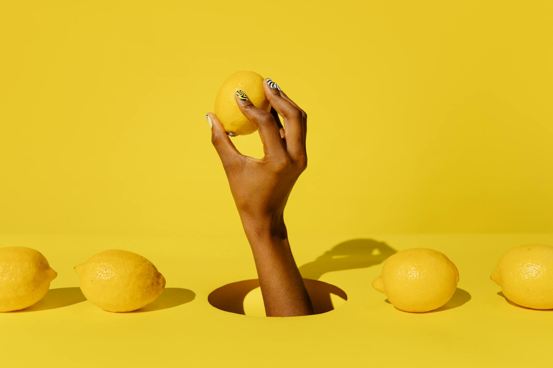 A hand holding a fresh lemon against a bright yellow background, symbolizing the bright clarity that comes with honest conversations about desire
