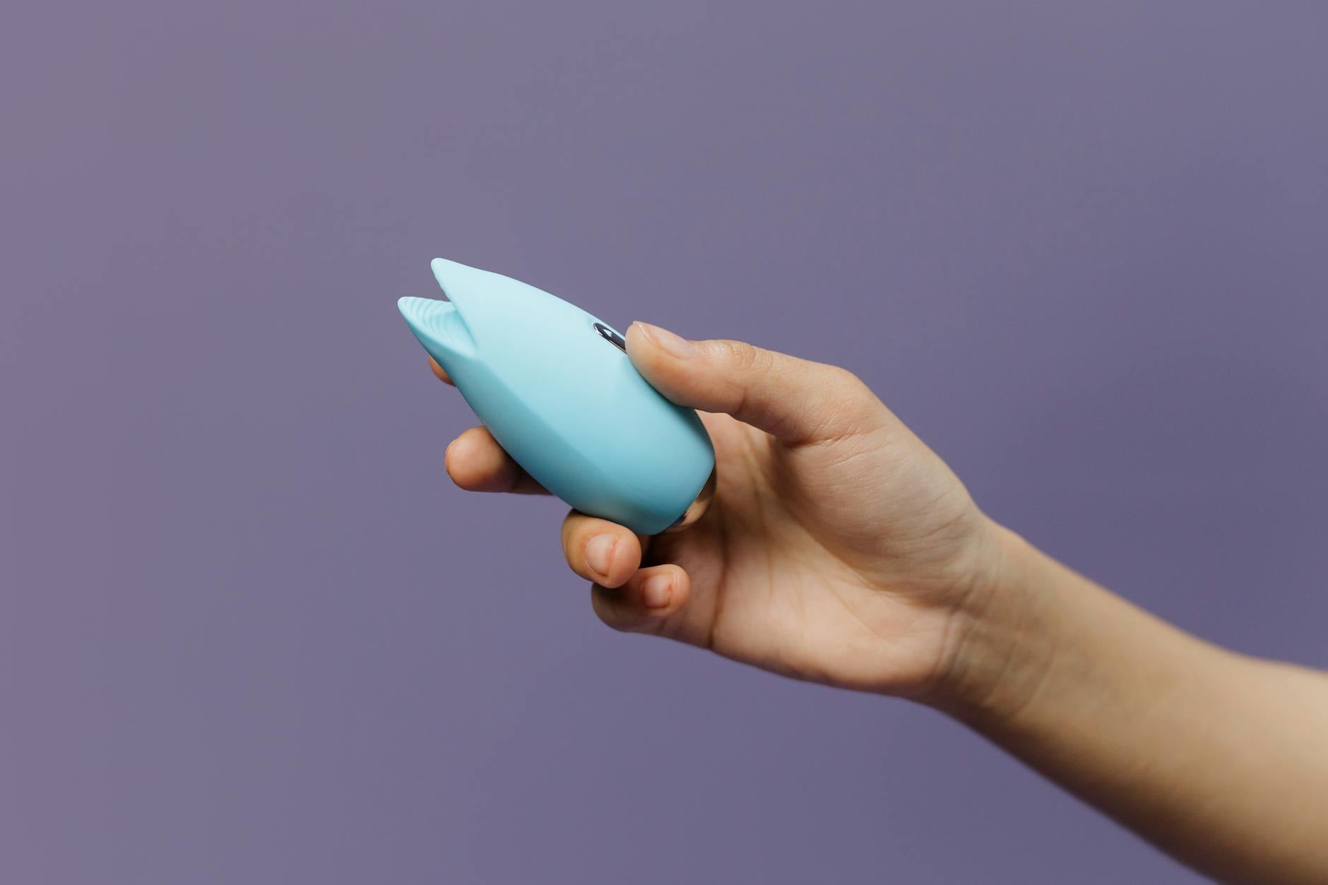 A hand holding a blue silicone vibrator against a purple background, symbolizing personal pleasure and self-care